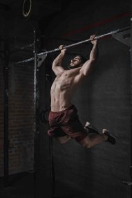Young crossfit athlete doing pull-ups at the gym. Handsome man doing functional training. Practicing calisthenics.